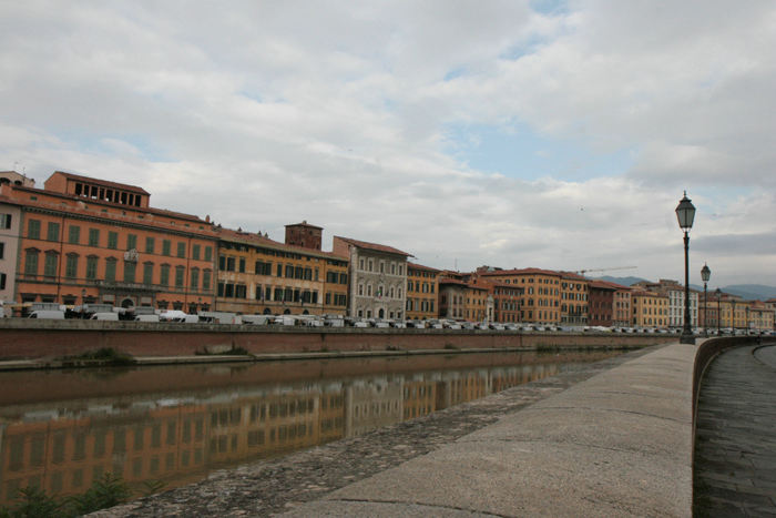 Bebyggelsen i Pisa langs Arno floden. Der var markedsdag i byen. De hvide varevogne, der holder i en lang række på den anden side af floden, var markedsfolk - der var rigtig mange.   