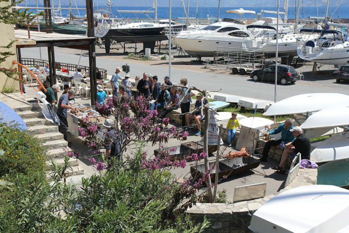 Agios Nikolaos påskedag. Kødet er stegt og ved at blive parteret, og folk er ved at samles til påskemiddagen i marinaen.