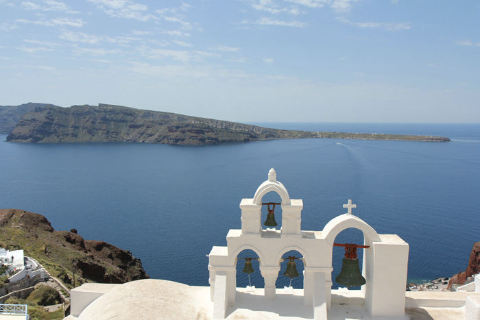 Kirkeklokker på en kirke i Oia med udsigt ud over vulkankrateret. 