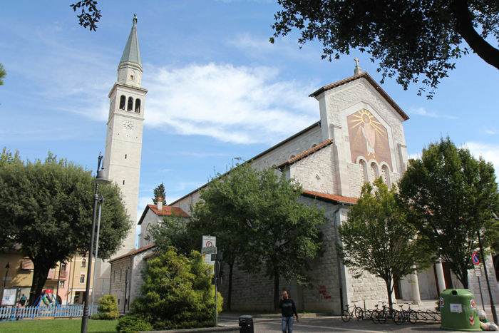 Kirken i Monfalcone. Klokketårnet i forbindelse med kirken er meget højt, og det er ikke kun i Monfalcone. Det er generelt for hele området, at kirkerne har meget høje klokketårne.