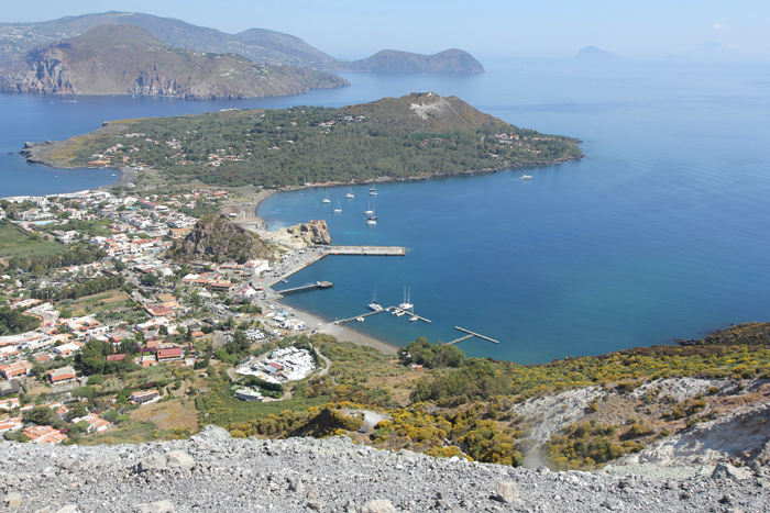 Udsigten oppe fra krateret på Vulcano ned over havnen. Vi ligger på indersiden af pontonbroen. Yderst til højre skimtes Panarea og Stromboli. 