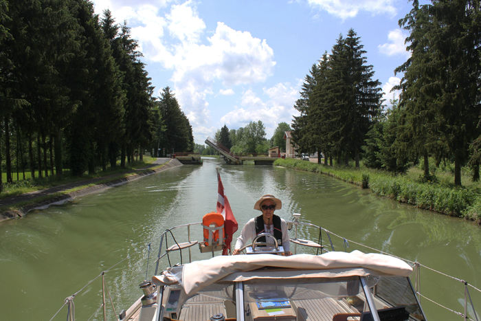 Skipperinden ved roret på Canal entre Champagne et Bourgogne. Vi må indrømme, at vi manglede en bom til at hænge vort solsejl op i eller en bimini, men vi klarede os med en bredskygget hat. 