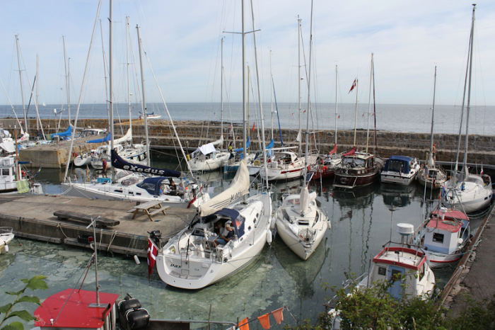 Gudhjem Havn set oppe fra toppen af klippen bag havnen. I forgrunden ses Pax, og i baggrunden ude ved ydermolen skimtes Nausikaa.