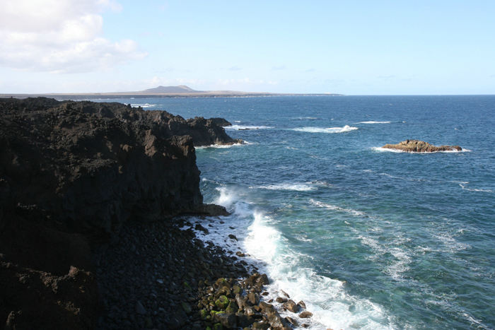 Los Hervideros på vestkysten af Lanzarote, en meget barsk og forrevet kyststrækning, flot med brændingen ind mod kysten. I baggrunden ses nordspidsen af Fuerteventura. 